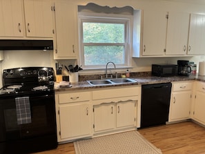 A kitchen with white cabinets, a black stove, a sink, and a window.