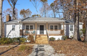 A single-story house with a front porch, a brick chimney, and a gravel driveway.