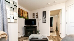 A living room with a fireplace, a television, and a hallway leading to a bedroom. - What a view!  (Victoria)