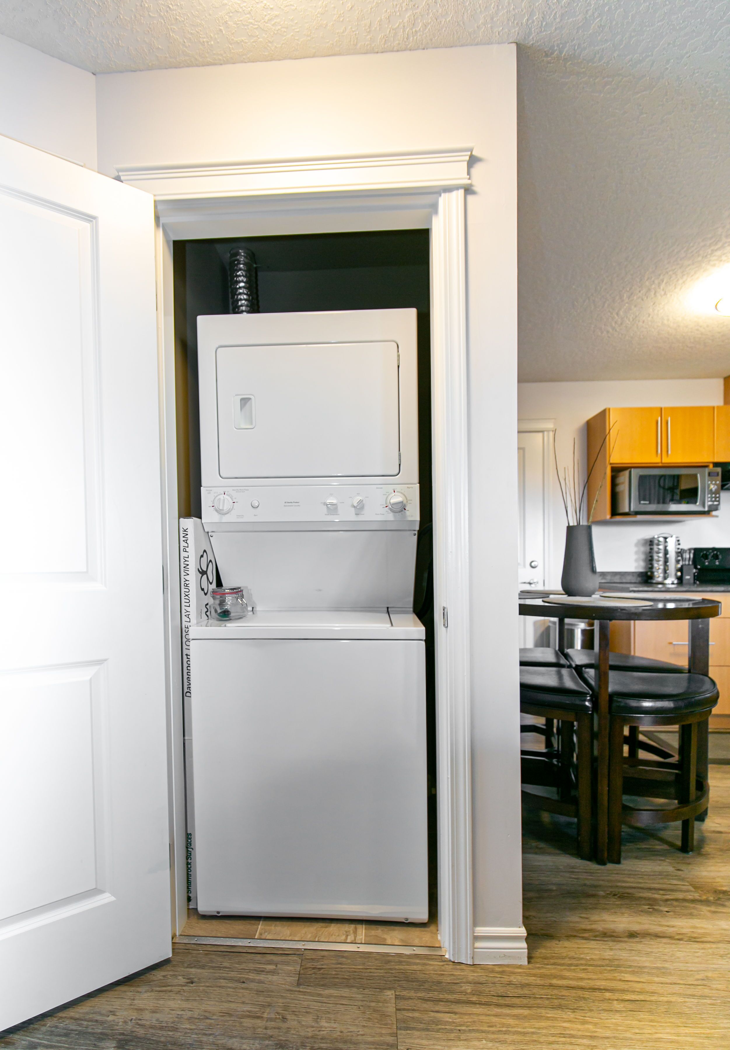 A compact kitchen with a built-in washer and dryer, wooden cabinets, a dining table with chairs, and a microwave.