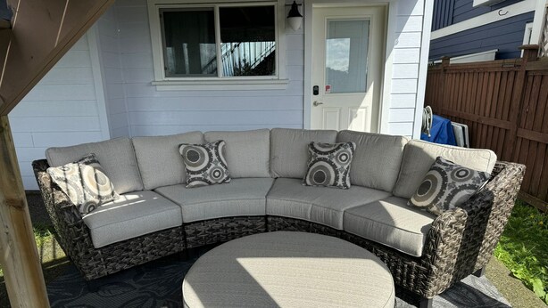 A curved sectional sofa with patterned cushions, a round ottoman, and a wicker accent chair, all set on a patterned outdoor rug. - What a view!  (Victoria)