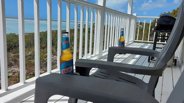 A covered outdoor area with white railings, a view of the ocean, and two Kalik beer bottles on a table.