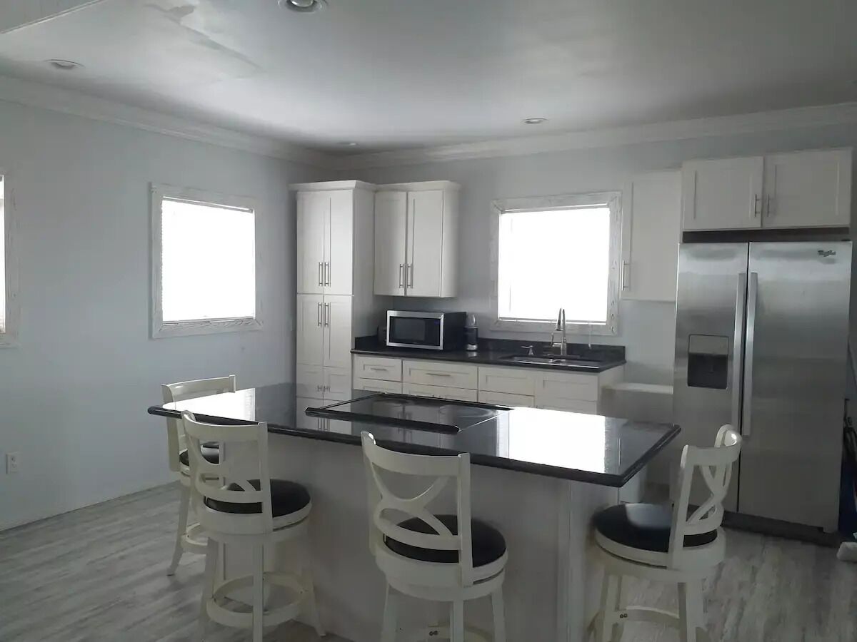 A modern kitchen with white cabinets, a central island with bar stools, a refrigerator, and a microwave.
