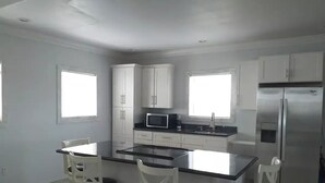 A modern kitchen with white cabinets, a central island with bar stools, a refrigerator, and a microwave.