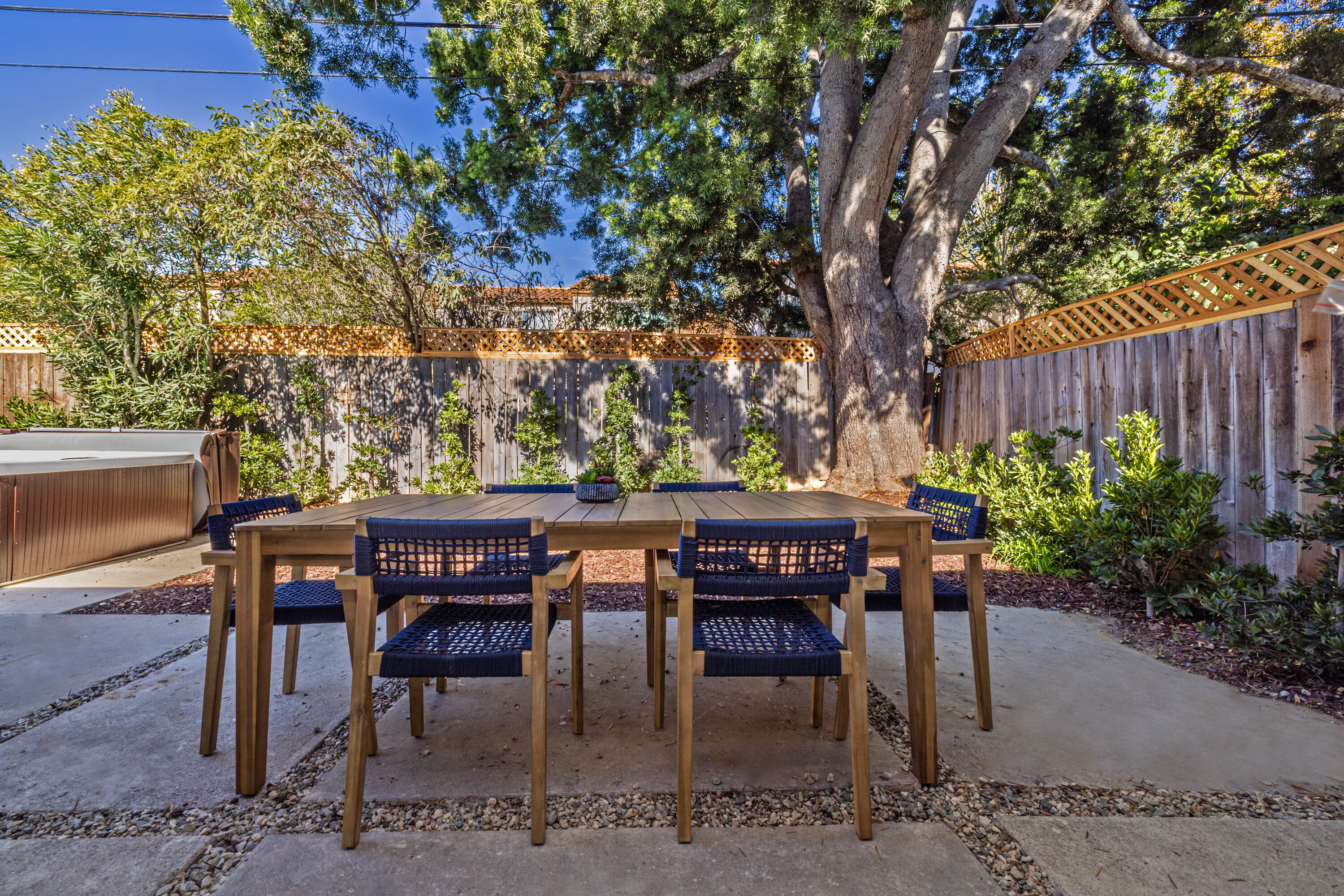 An outdoor patio with a wooden table and chairs, surrounded by a wooden fence and trees.