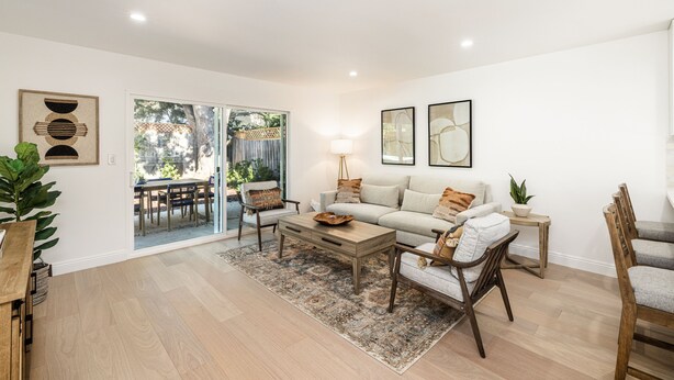 A living room with a sofa, coffee table, and chairs, a dining area with a table and chairs, and a large window with a view of the outdoors. - Two Bedroom Home Near Beach (Santa Barbara) (Santa Barbara)