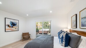 A bedroom with a large bed, a bench, and a sliding glass door leading to an outdoor area. - Two Bedroom Home Near Beach (Santa Barbara) (Santa Barbara)