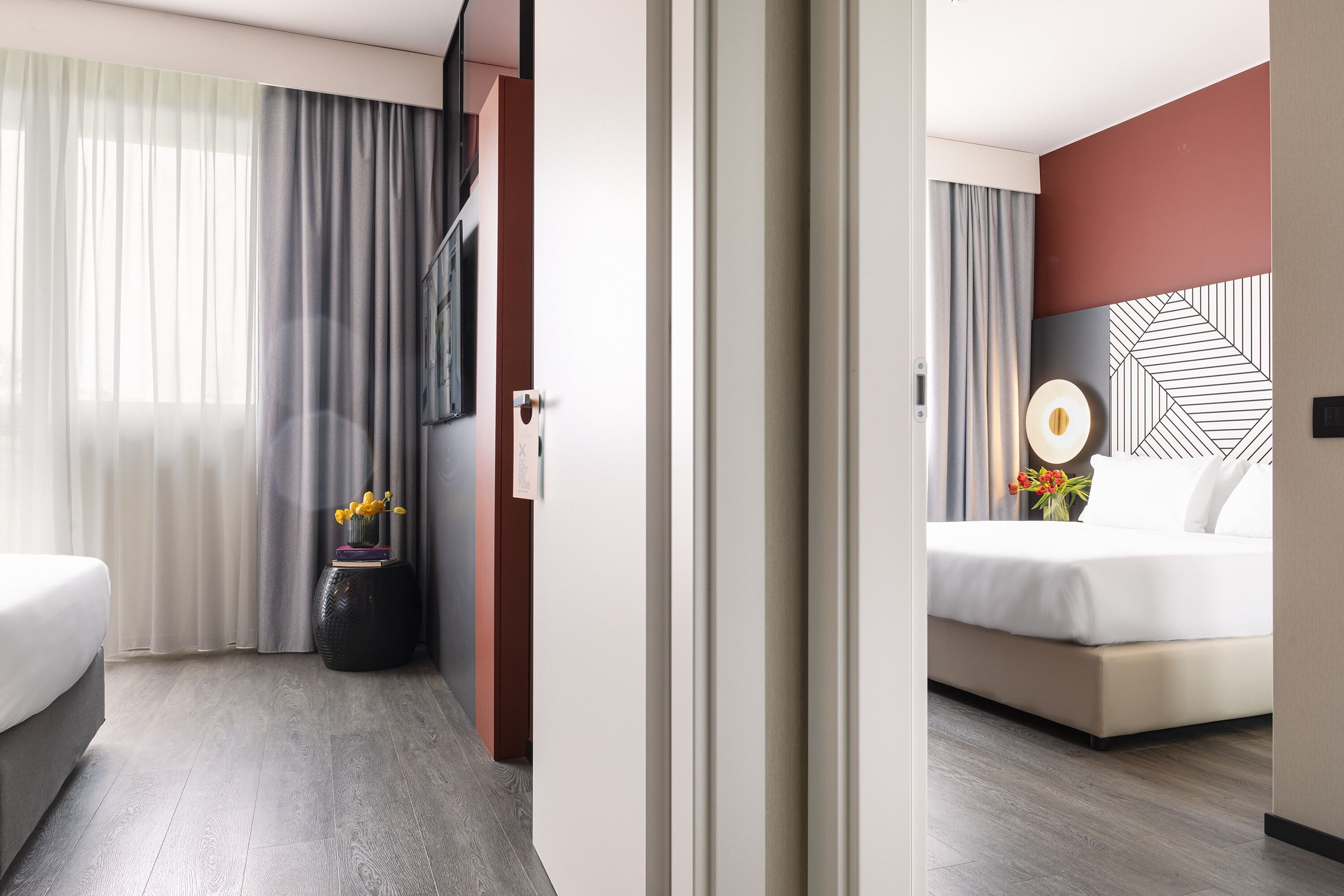 A hotel room with a bed, a nightstand, a wall-mounted TV, and a window with curtains.