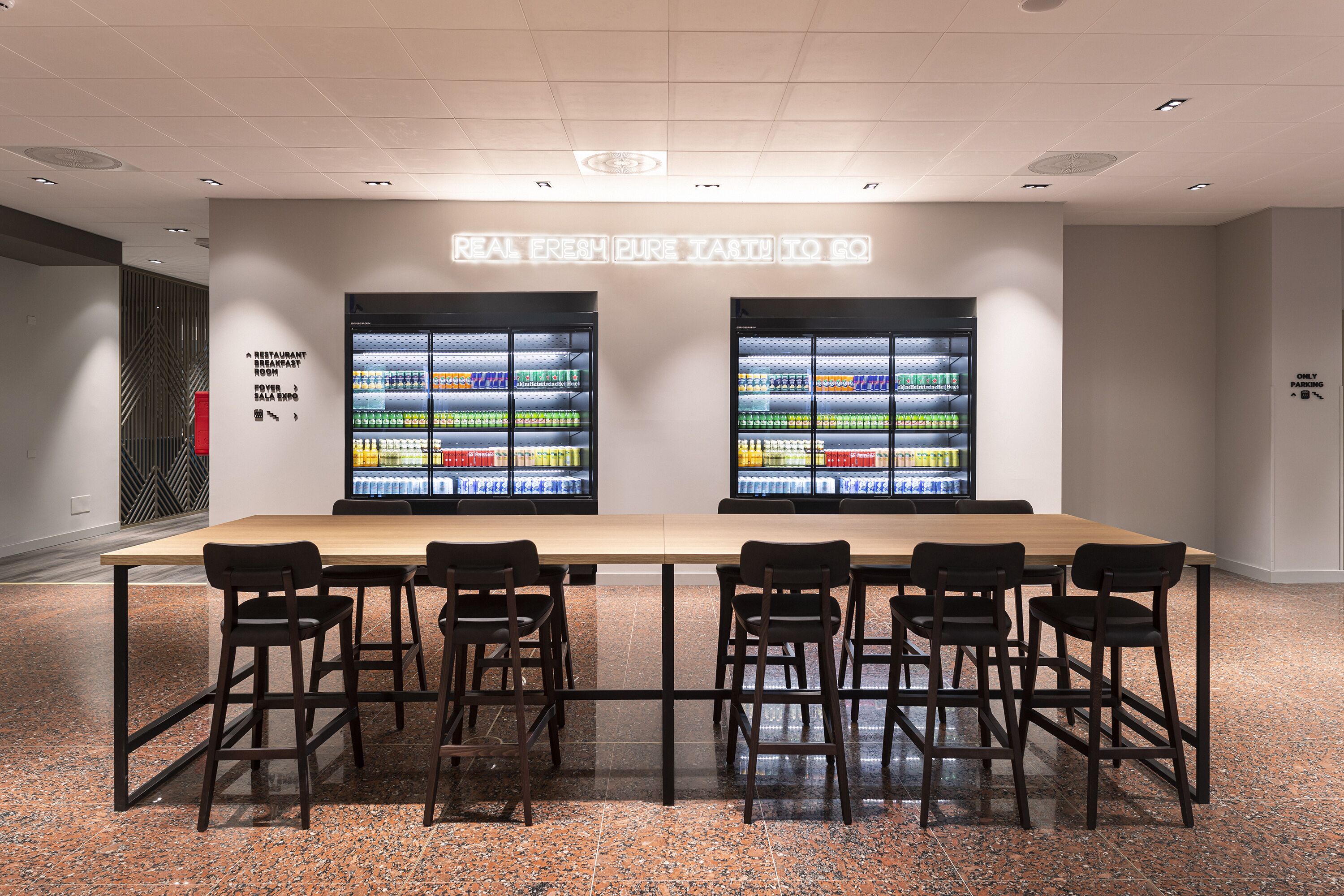 A restaurant with a long table and chairs, two refrigerators stocked with beverages, and a sign indicating a restaurant and a food expo.