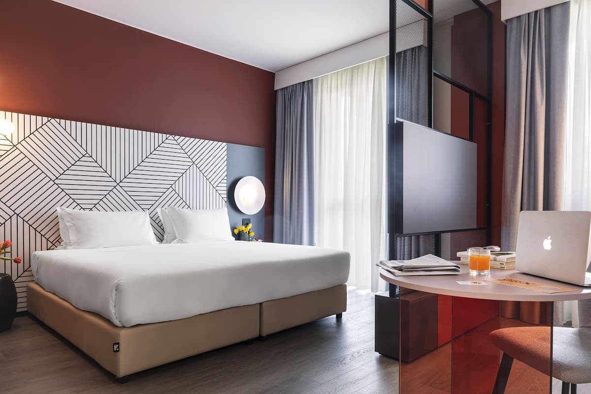 Moderni hotellihuone, jossa on suuri sänky, työpöytä kannettavalla tietokoneella ja televisio.