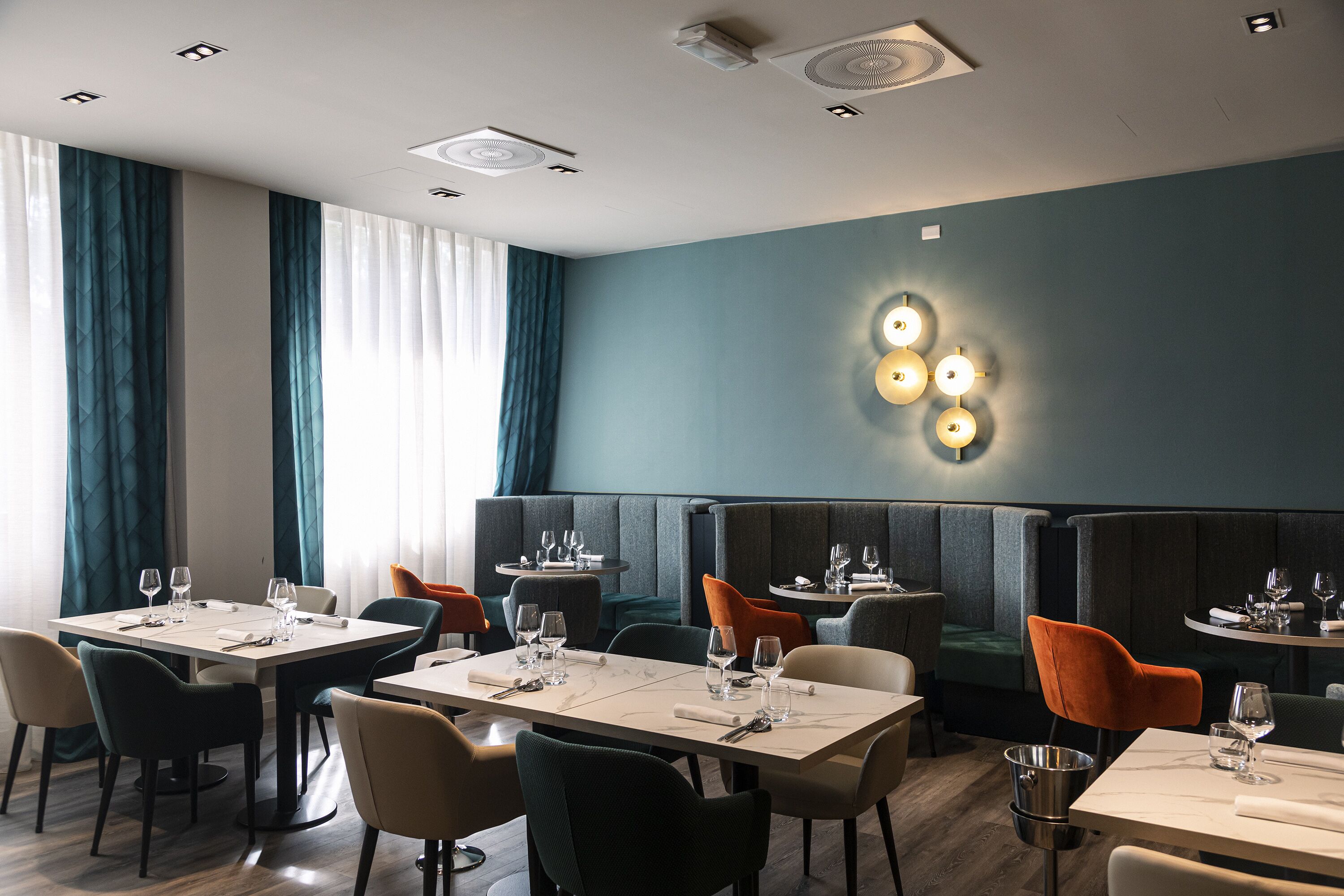 A modern restaurant with booths and tables, a blue accent wall, and a chandelier.