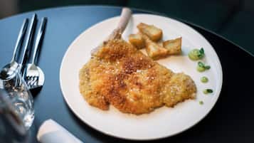 Un plato con una escalope empanizada y frita, acompañado de patatas asadas y guisantes verdes, sobre un plato blanco.