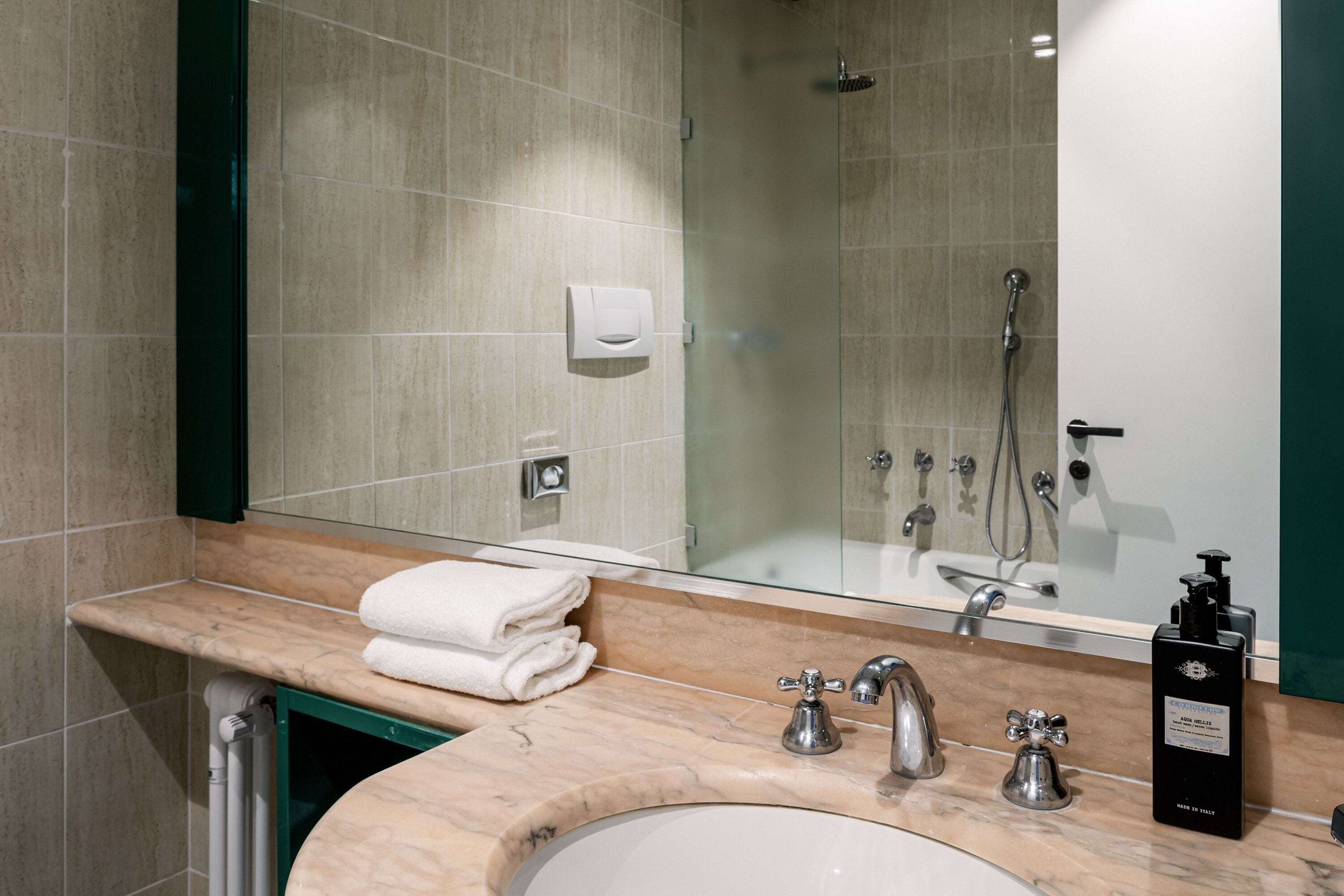 A bathroom with a marble sink, a mirror, a glass shower enclosure, and a towel dispenser.