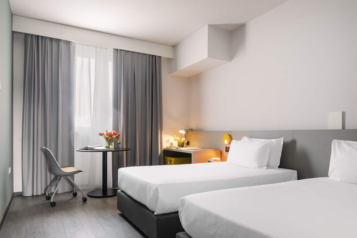 Hotellihuone, jossa on kaksi sänkyä, työpöytä ja tuoli.
