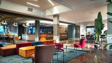 A modern lobby with a bar area, seating arrangements, and a large plant.