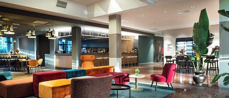 A modern lobby with a bar area, seating arrangements, and a large plant.