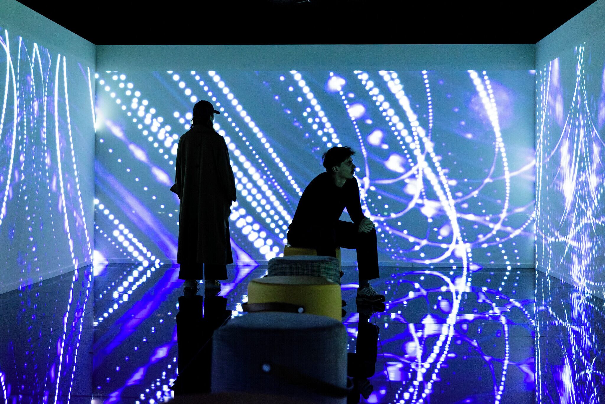 A room with a reflective floor and a large LED screen displaying abstract patterns.