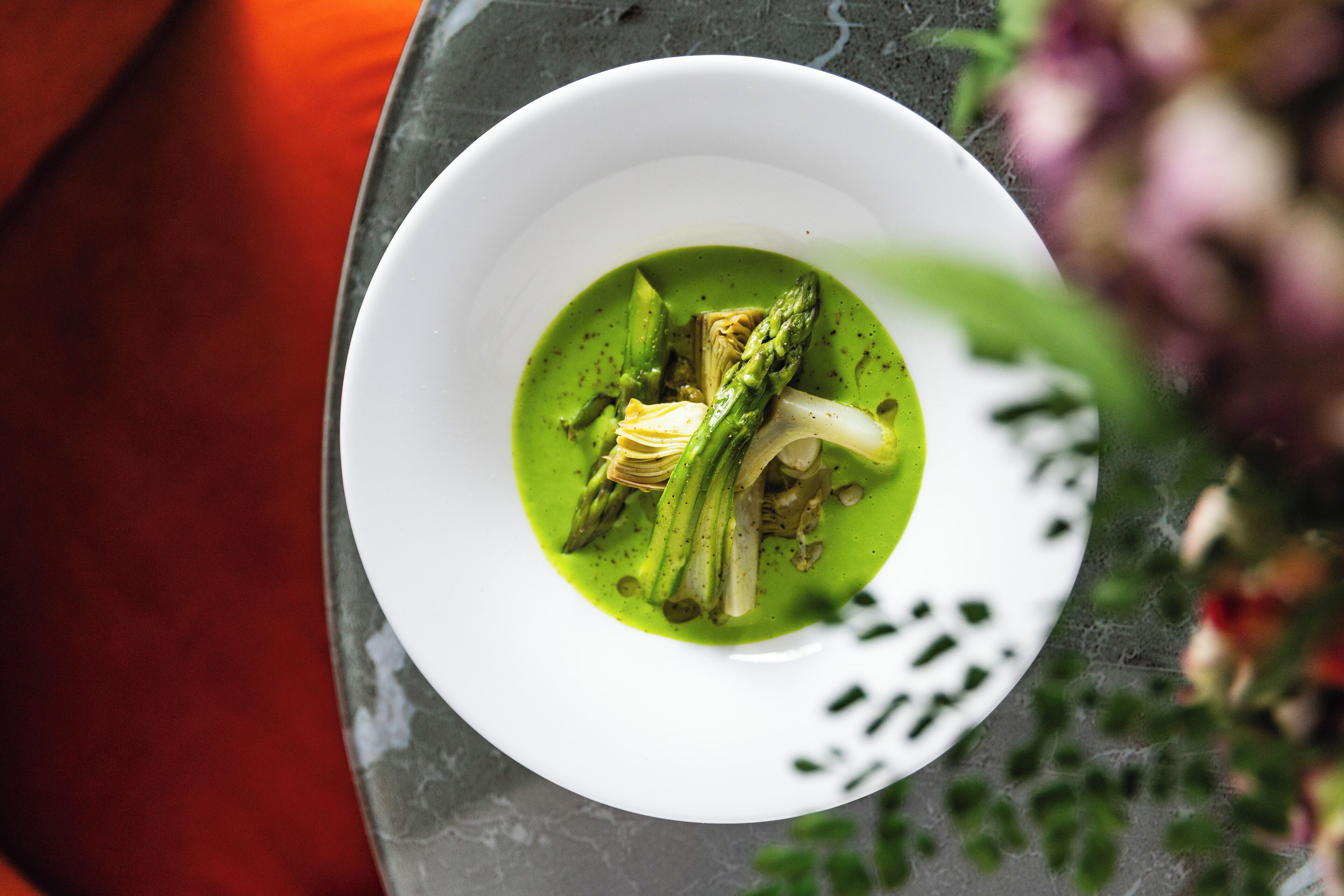 Un tazón blanco con sopa verde y verduras sobre una superficie oscura.