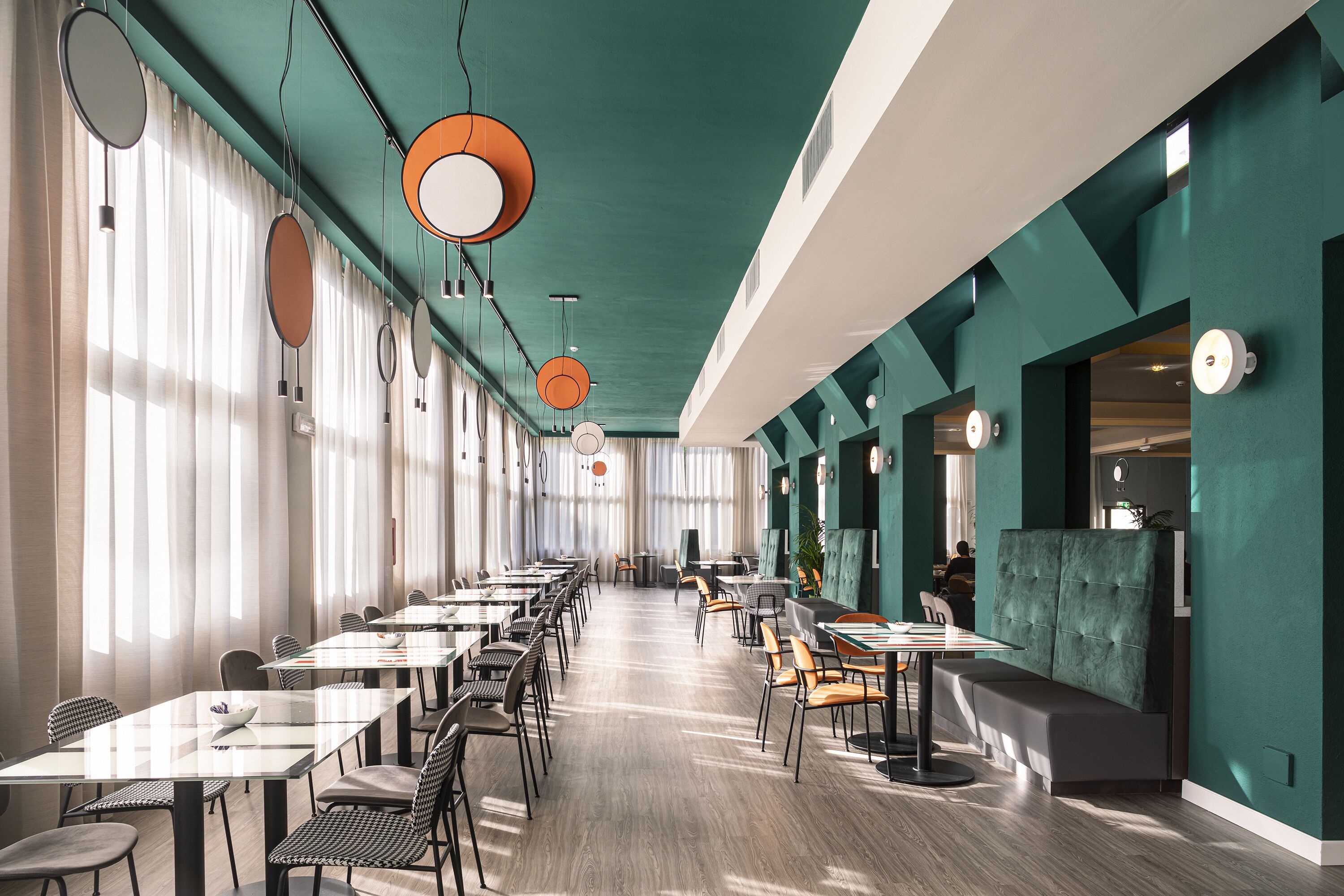 Un restaurante espacioso con mesas y sillas largas, ventanas amplias y un techo color turquesa.