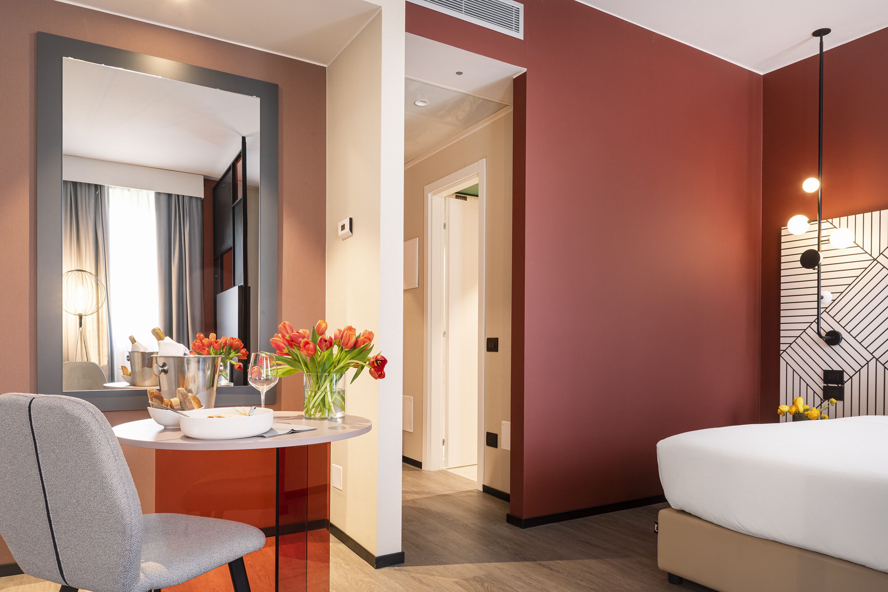 A hotel room with a bed, a dining table with a vase of flowers, a chair, and a mirror.