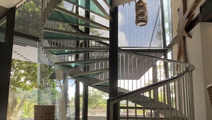 Een modern interieur met een wenteltrap, een rieten stoel en uitzicht op groen buiten.