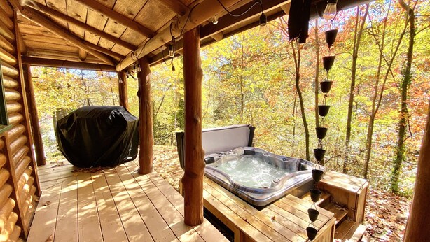 A wooden deck with a hot tub, surrounded by trees with autumn foliage.