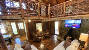 A spacious living room with a high ceiling, wooden beams, a fireplace, a television, and a cozy seating area.