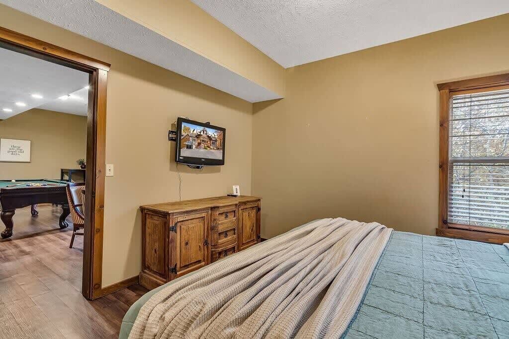 Une chambre à coucher comprenant un lit, un téléviseur fixé au mur, une commode en bois et une porte donnant sur une autre pièce.