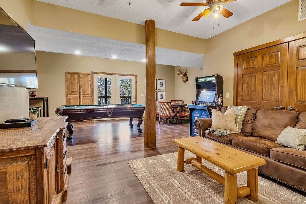 A spacious living room with a pool table, a wooden bench, a brown leather couch, and a television.