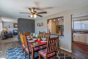 A dining area with a wooden table set for four, surrounded by chairs with plaid cushions. A ceiling fan is visible above the table, and a stone wall is behind the seating area. - The Farmhouse by Host Boise - Pet Friendly Home and Garage near Fairgrounds (Boise)