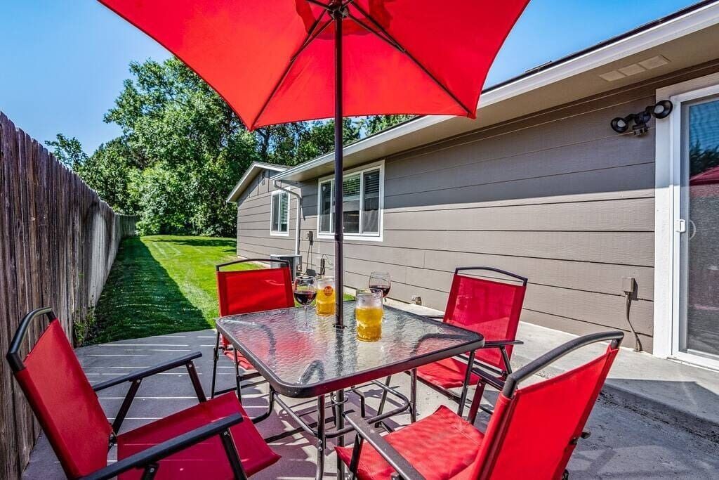 Eine Terrasse mit einem Glastisch und roten Stühlen, einem roten Sonnenschirm und einem Haus im Hintergrund.