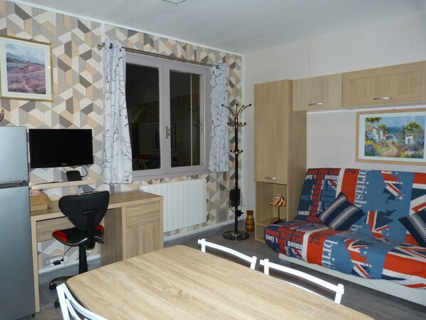 A compact living space with a dining table, a sofa with a British flag pattern, a television, and a window with curtains.