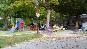 Une aire de jeux avec des toboggans et des structures d’escalade, entourée d’arbres et de tables de pique-nique.