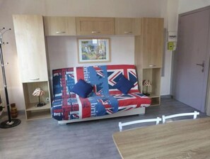 A compact room with a sofa bed featuring a Union Jack design, wooden cabinets, a small table, and a framed picture on the wall.