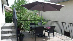 Une terrasse extérieure avec une table et des chaises, un grand parasol et un escalier menant à un niveau supérieur.