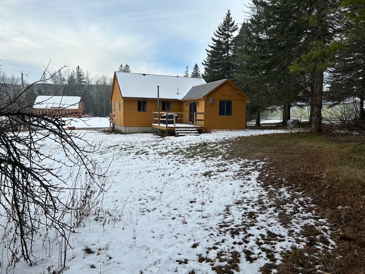 Uma cabana de madeira com varanda, rodeada por neve na terra e nas árvores.