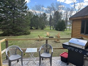 A deck with a grill, two Adirondack chairs, and a small table.