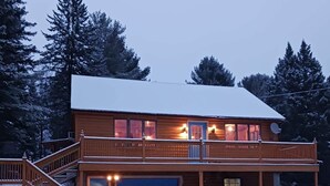 A two-story wooden cabin with a covered porch, a garage, and a staircase leading to the upper level. - Cozy Errol Home conveniently close to town and with snowmobile access!  (Errol)
