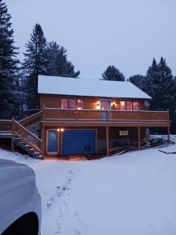 A two-story wooden cabin with a covered porch, a garage, and a staircase leading to the upper level.