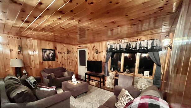 A cozy log cabin interior with a sofa, ottoman, and a television. - Cozy Errol Home conveniently close to town and with snowmobile access!  (Errol)