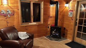 A cozy cabin interior with a leather chair, a wood-burning stove, and a large window. - Cozy Errol Home conveniently close to town and with snowmobile access!  (Errol)