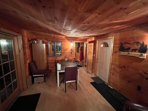 A wooden cabin interior with a dining table and chairs, a refrigerator, and a coat rack.