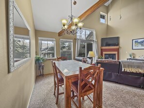 A dining area with a wooden table and chairs, a chandelier, and large windows with curtains.