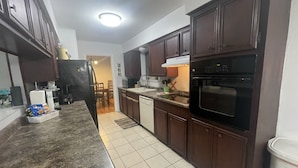 Una cocina con armarios de madera oscura, un refrigerador negro, un microondas, una estufa y un lavavajillas.