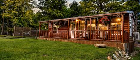 A log cabin with a porch, surrounded by a grassy yard and trees.
