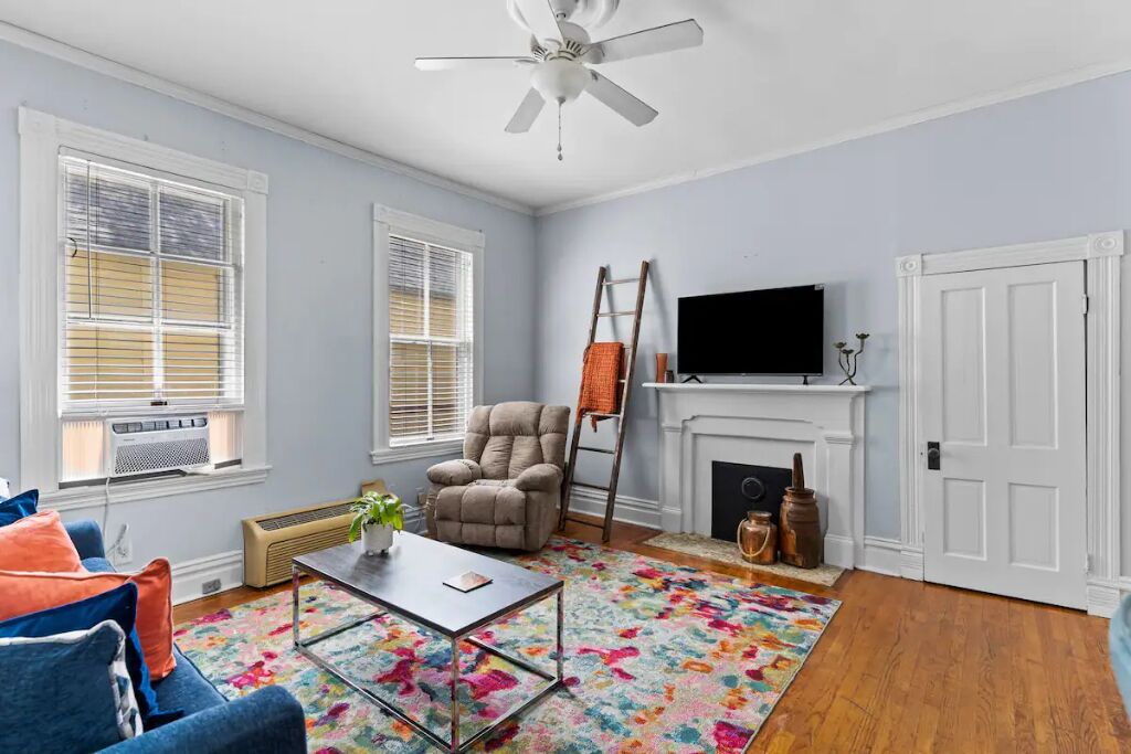 A living room with a ceiling fan, a fireplace, a television, and a colorful rug.