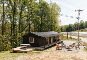 A cabin with a deck and picnic table, surrounded by trees and a road. - Cozy Dumplin' RRG - Warm & Modern Stay in RRG/Auxier (Pine Ridge)