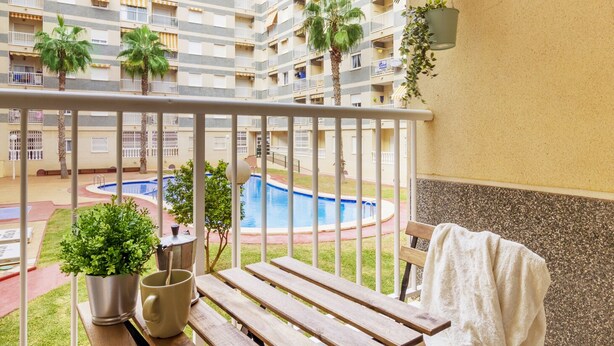 A balcony with a pool, potted plants, and a bench. - Pink Sunshine beach apartment (Torrevieja)