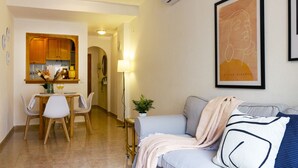 A living room with a sofa, a dining area with a table and chairs, and a kitchen with wooden cabinets. - Pink Sunshine beach apartment (Torrevieja)