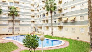 A multi-story hotel with a central swimming pool, surrounded by well-maintained grass and palm trees. - Pink Sunshine beach apartment (Torrevieja)